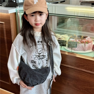Kids black denim crescent crossbody bag with orange tag worn by a child in a bakery