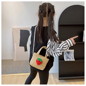 Rear view of child wearing straw shoulder bag with plush strawberry decoration
