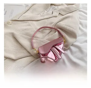 Detail view of pink mirror leather saddle bag with gold buckles on a beige texture