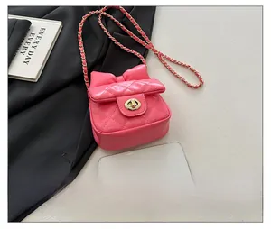 Pink quilted mini crossbody bag with a large bow shown next to a smartphone for size
