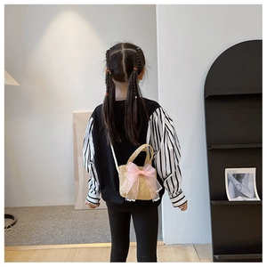 Detail of child wearing straw mini crossbody bag with pink bow and pearl charms