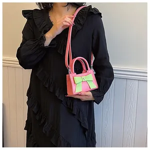 Dettaglio mini borsa rosa con fiocco verde, fibbia a cuore e tracolla sottile rimovibile