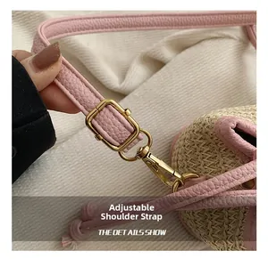 Détail de la bandoulière réglable en cuir rose avec boucle dorée sur un sac en paille