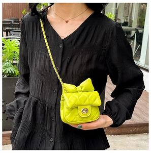 Detail of neon yellow quilted mini bag with bow decoration and gold chain strap