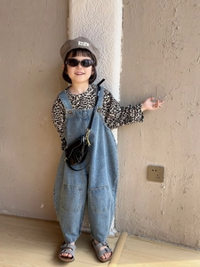 Detail of trendy black glossy mini saddle bag worn with denim overalls and leopard shirt