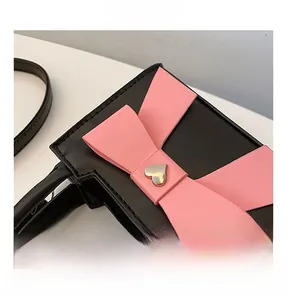Dettaglio di una borsa a tracolla in ecopelle nera con fiocco rosa e fibbia a cuore