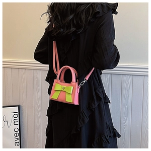 Mini borsa rosa con fiocco verde e fibbia a cuore indossata su un abito nero da modella