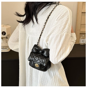 Close-up of black quilted mini bag featuring a large bow and gold chain strap