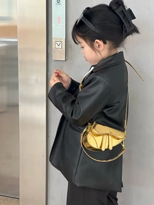 Detail of a shiny metallic gold kids' saddle bag worn by a model in a trendy outfit