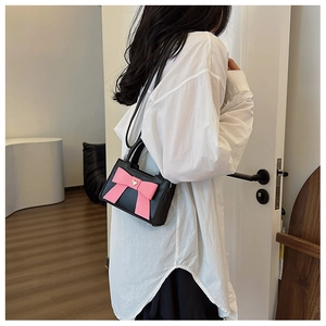 Dettaglio di una borsa nera per bambini con grande fiocco rosa e ciondolo a cuore