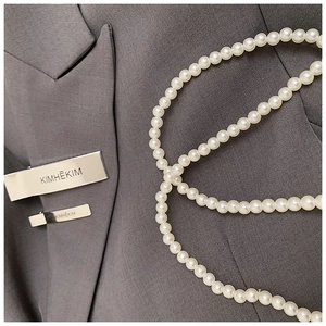 Detail of multi-layered white pearl accessory on a dark grey tailored jacket