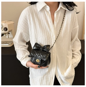 Detail of black quilted mini bag with oversized bow and golden turn-lock closure