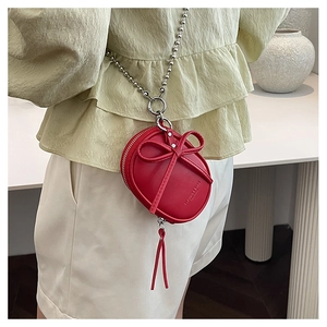 Mini bolso redondo rojo con lazo y cadena plateada sobre ropa de color claro