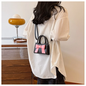 Ragazza indossa mini borsa a tracolla nera con fiocco rosa e ciondolo a cuore dorato