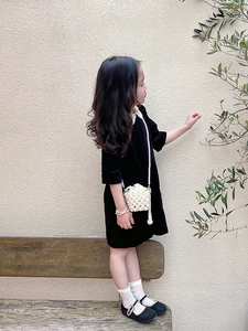 Detail of a pearl woven crossbody bag paired with a black velvet dress and Mary Jane shoes