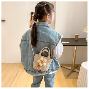 Detail view of kids woven straw crossbody bag with plush yellow flower and cherry charms