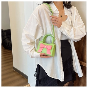 Dettaglio borsa verde pastello con fiocco rosa su camicia bianca e gonna di pizzo