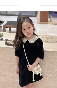 Detail of child wearing a black corduroy dress with white lace collar and pearl purse