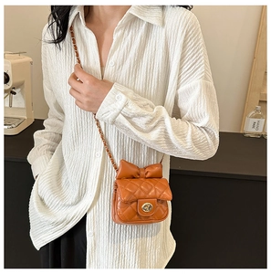 Detail of orange quilted crossbody bag with leather bow and metallic twist lock strap