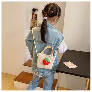 Toddler wearing a cream handmade straw shoulder bag with a 3D strawberry charm
