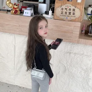 Girl's shiny silver sequin mini crossbody bag with a metal chain strap in a cafe setting