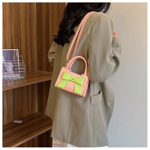 Dettaglio mini borsa rosa con fiocco verde neon indossata su un blazer chiaro