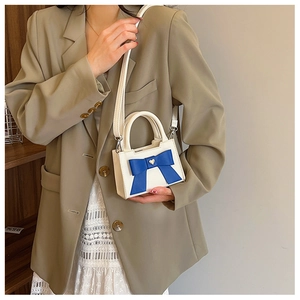 Dettaglio di mini borsa bianca con fiocco blu e cuore dorato in pelle PU testurizzata