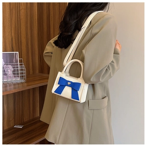 Dettaglio della mini borsa bianca con fiocco blu e ciondolo a cuore sulla tracolla sottile