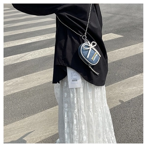 Detalle de un mini bolso bandolera redondo de mezclilla azul con lazo blanco y parche arcoíris