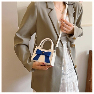 Dettaglio mini borsa in pelle bianca con fiocco blu e ciondolo a cuore dorato