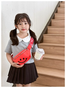 Close-up of a red kids' waist bag with a black smiley face worn by a girl on stairs