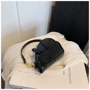 Detail of glossy black patent leather saddle bag with gold metal hardware on white fabric