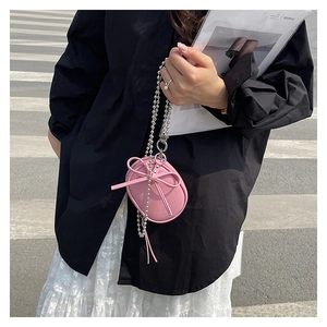 Detalle de un mini bolso rosa bandolera con lazo 3D y cadena de bolas metálicas plateadas