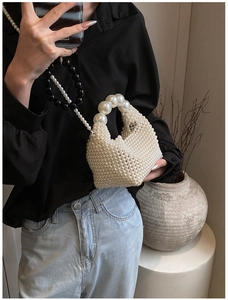 Close-up of a handmade pearl woven handbag with a decorative black and white beaded strap