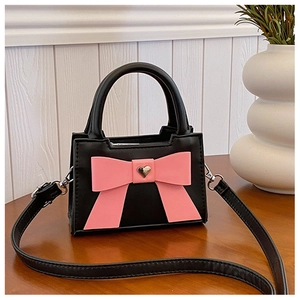 Dettaglio della borsa a tracolla nera per bambini con grande fiocco rosa e fibbia a cuore