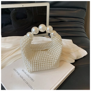 Detail of hand-woven pearl handbag featuring large pearl handle on silk background