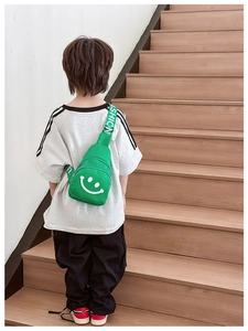 Rear view of a child wearing a bright green nylon chest bag with a white smiley face