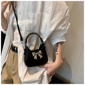 Détail du mini sac noir avec un grand nœud métallique argenté sur du cuir synthétique lisse