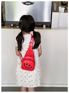 Close-up of red nylon kids' crossbody bag featuring a smiling face and lettered strap