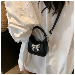 Mini sac à main noir tendance avec grande boucle en nœud doré porté par un mannequin