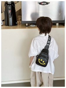 Detailed view of kids' black chest bag featuring a yellow smiley face and lettered strap