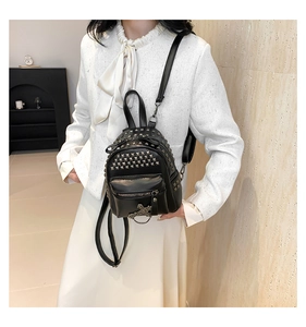 Detail of black mini backpack with gold rivets and metallic cross charm on a model