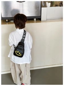 Close-up of black leather kids chest bag featuring a yellow smiley and logo strap