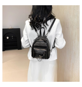 Detail of punk style black mini backpack with silver rivets and metal cross charms on model
