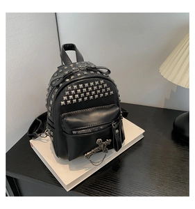 Close-up of a black punk backpack with silver square rivets and a cross chain charm