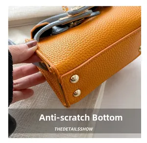 Close-up of orange litchi leather bag base featuring four golden protective metal studs