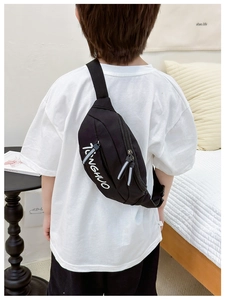 Detail of child wearing a black canvas chest bag with white letters and adjustable strap