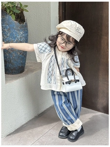 Detail of girls beige cotton top with blue embroidery and striped trousers outfit