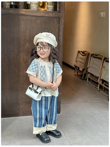 Detail of girls beige cotton top with embroidery and blue striped pants ensemble