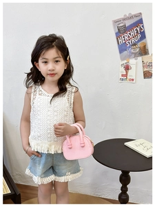 Mini borsa rosa a grana portata da una bambina con top in pizzo bianco e pantaloncini denim